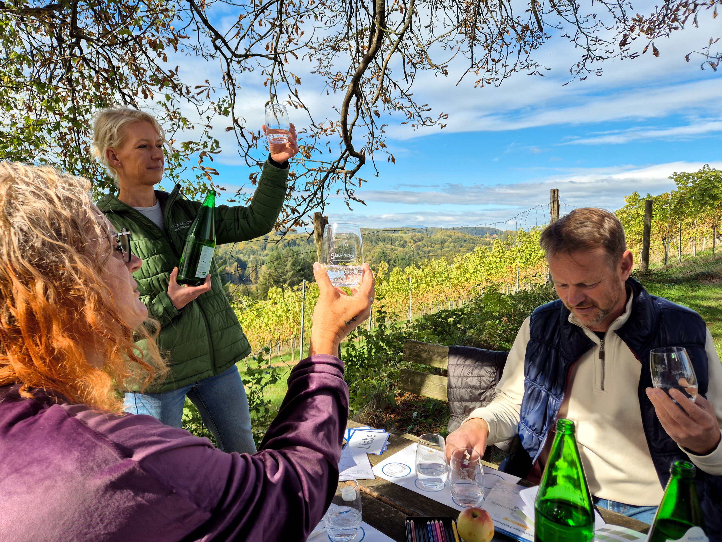 Drei Personen sitzen mit Wassergläsern am Tisch und verkosten