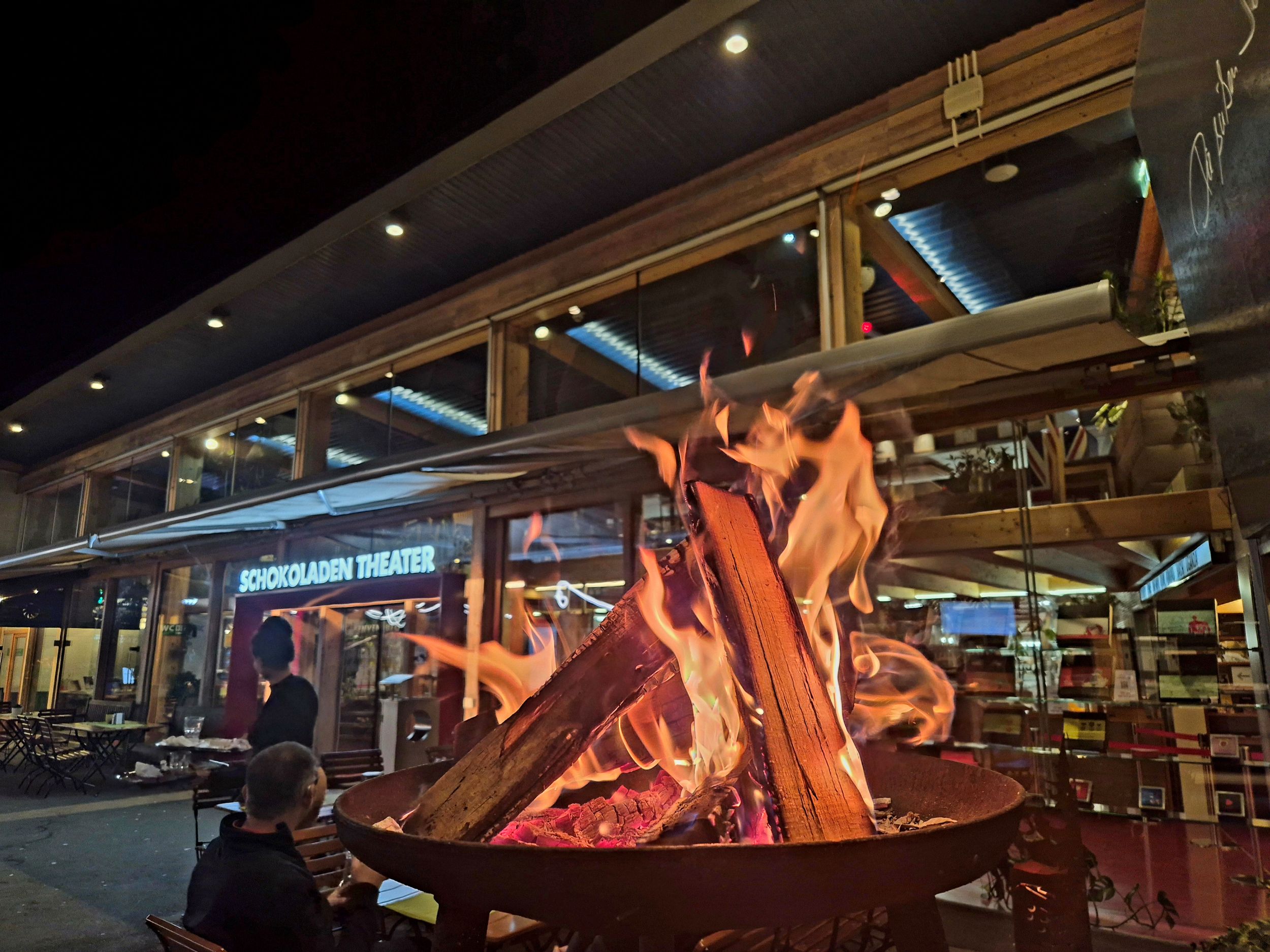 Es ist Nacht. Im Vordergrund brennt ein Lagerfeuer, im Hintergrund ist der Eingang zur Schoko-Fabrik Zotter erkennbar.