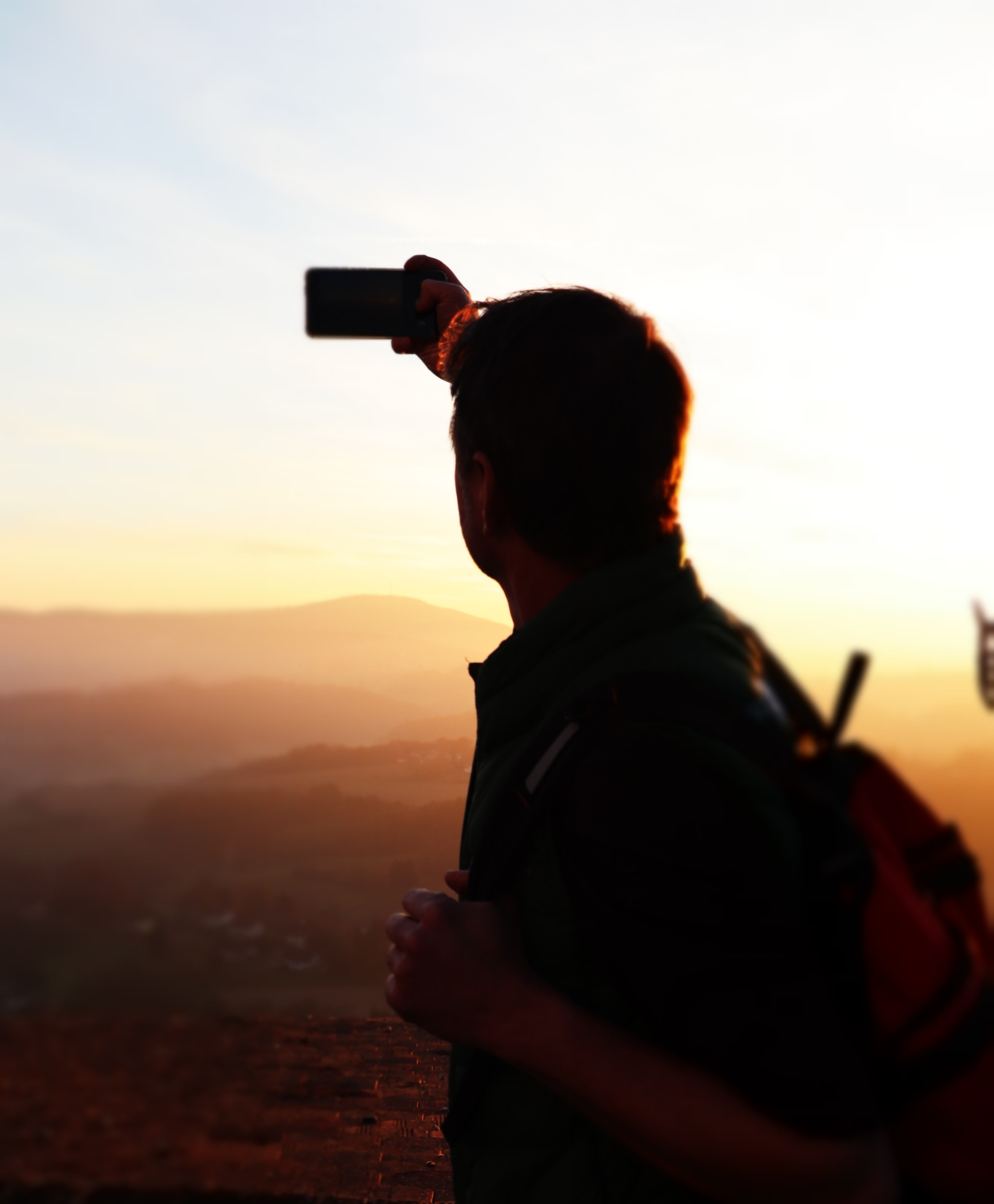 Ein Mann macht mit einem Smartphone ein Foto vom Sonnenuntergang