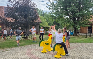 Mehrere Personen stehen am und in der Wiese um einen Hof und lachen gut gelaunt