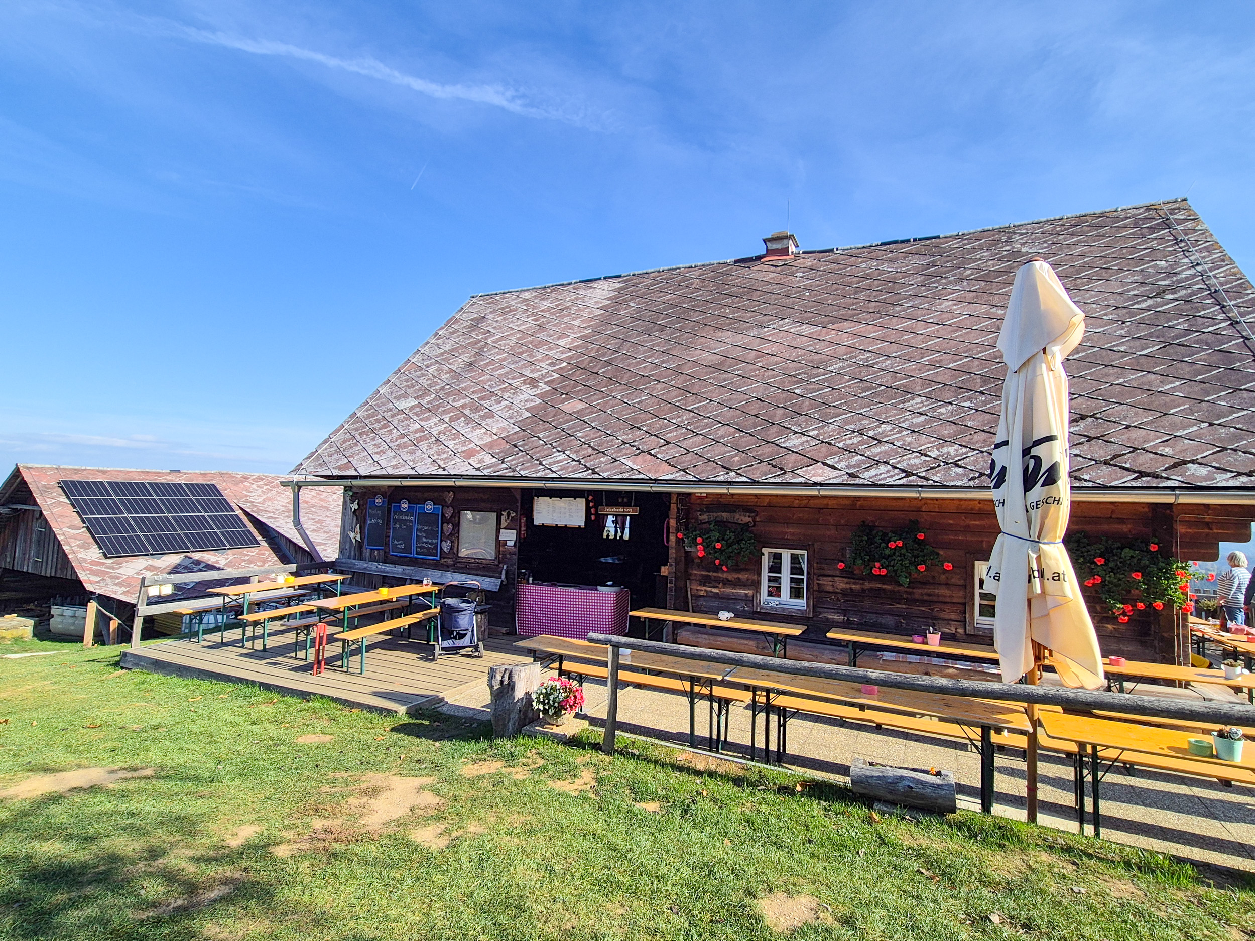 Wandern am Grenzpanoramaweg, Remschniggalm Vor einer rustikalen Holzhütte stehen Tische und Bänke
